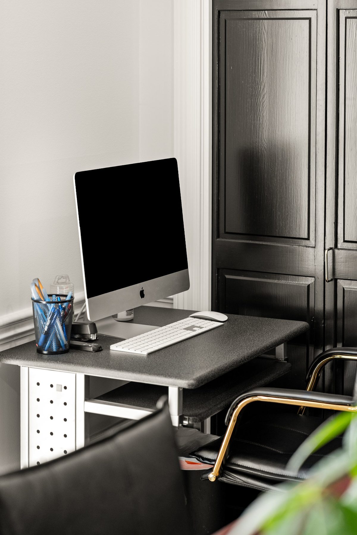 A desk tucked beside black-painted closet doors, gold-armed office chair in the foreground — photo by Jimmy Warr