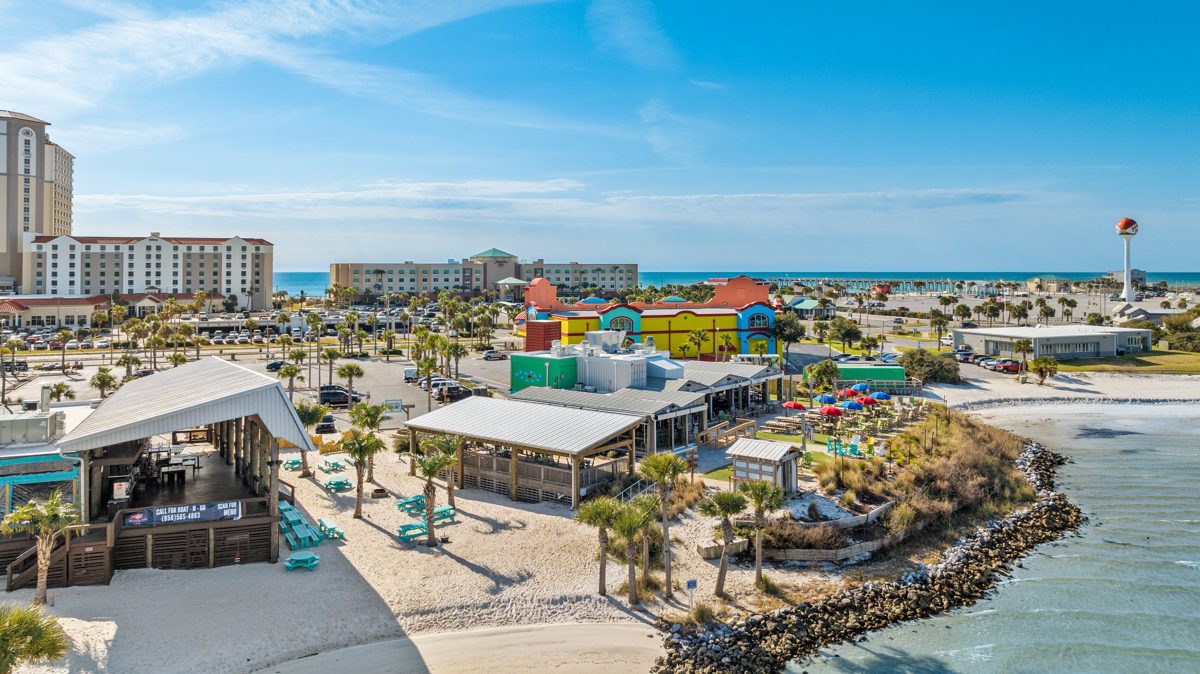 Red Fish Blue Fish from above the sound, with the Pensacola Beach pier, hotels, and beach-ball water tower behind — photo by Jimmy Warr