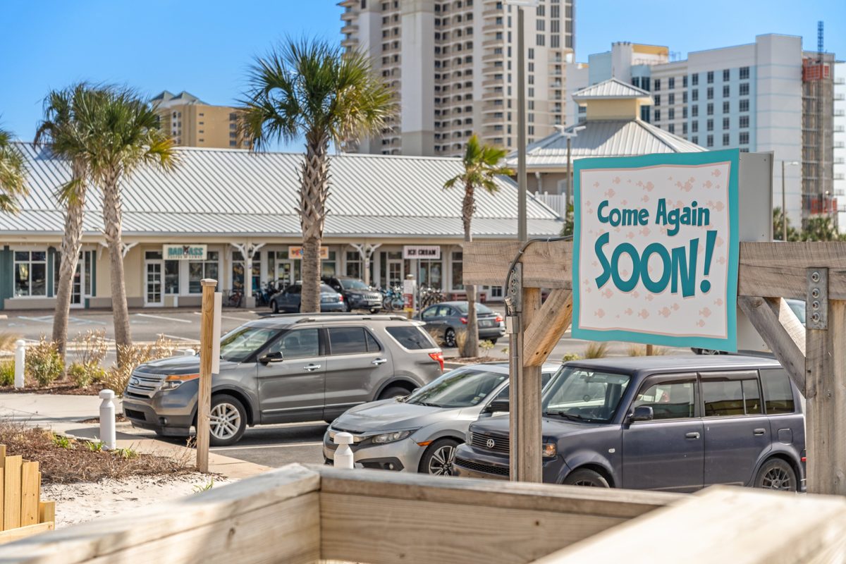 A Come Again Soon! sign at the exit, palms and the Pensacola Beach skyline behind — photo by Jimmy Warr