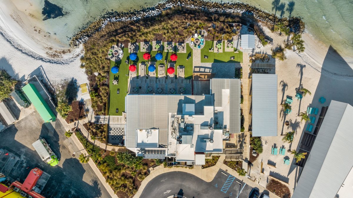 Straight-down drone view of Red Fish Blue Fish: rows of red and blue umbrellas on the lawn above the rock jetty — photo by Jimmy Warr
