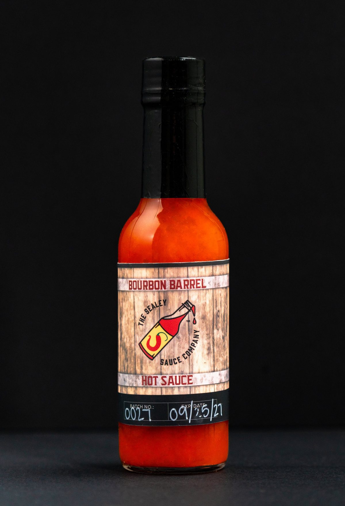 The Sealey Sauce Company Bourbon Barrel hot sauce with its wood-grain label, on black — photo by Jimmy Warr