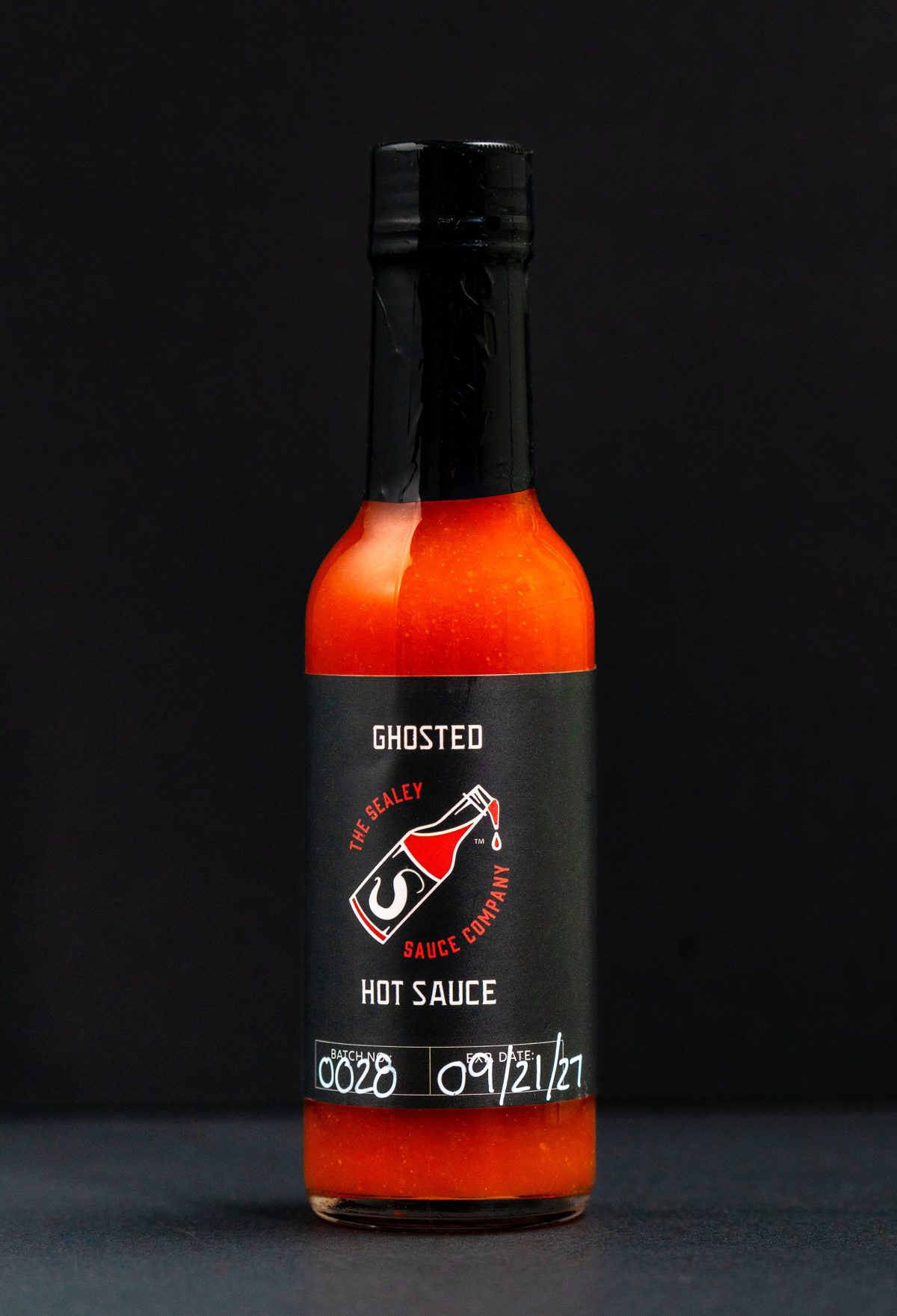The Sealey Sauce Company Ghosted hot sauce with its black label, on black — photo by Jimmy Warr
