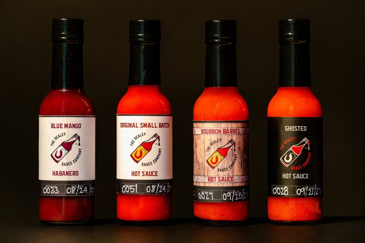 Four The Sealey Sauce Company bottles on black: Blue Mango Habanero, Original Small Batch, Bourbon Barrel, and Ghosted — photo by Jimmy Warr