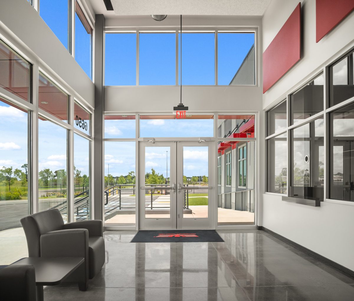 Two-story lobby with glass doors, red wall panels, and polished concrete floors — photo by Jimmy Warr