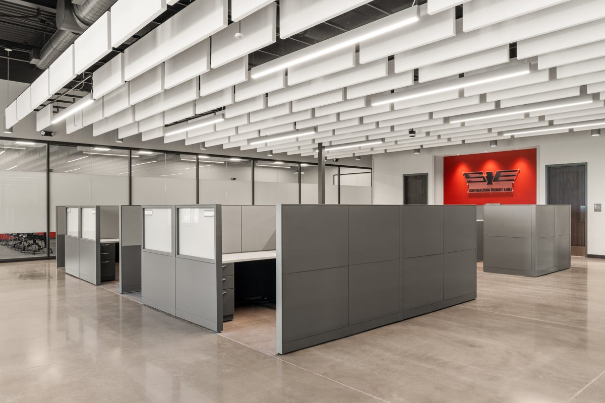 Open office under suspended white acoustic baffles, the company logo on a red wall — photo by Jimmy Warr
