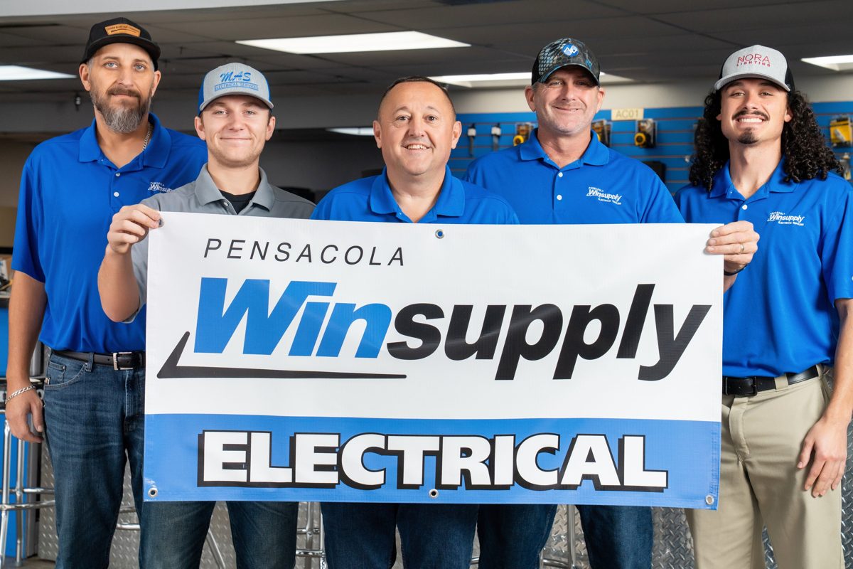 Tighter frame of the Pensacola Winsupply team smiling behind their Electrical banner — photo by Jimmy Warr