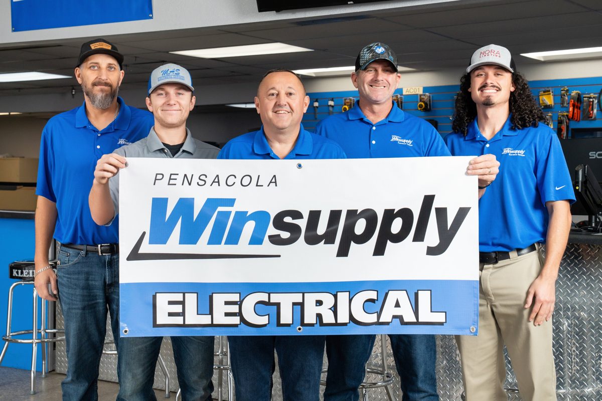 The Pensacola Winsupply team holds their Electrical banner in front of the sales counter and tool wall — photo by Jimmy Warr