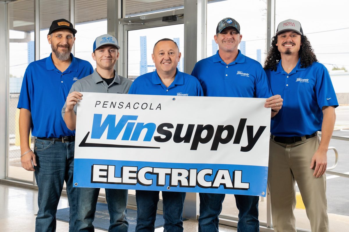 Five members of the Pensacola Winsupply team hold a Winsupply Electrical banner inside the glass storefront — photo by Jimmy Warr