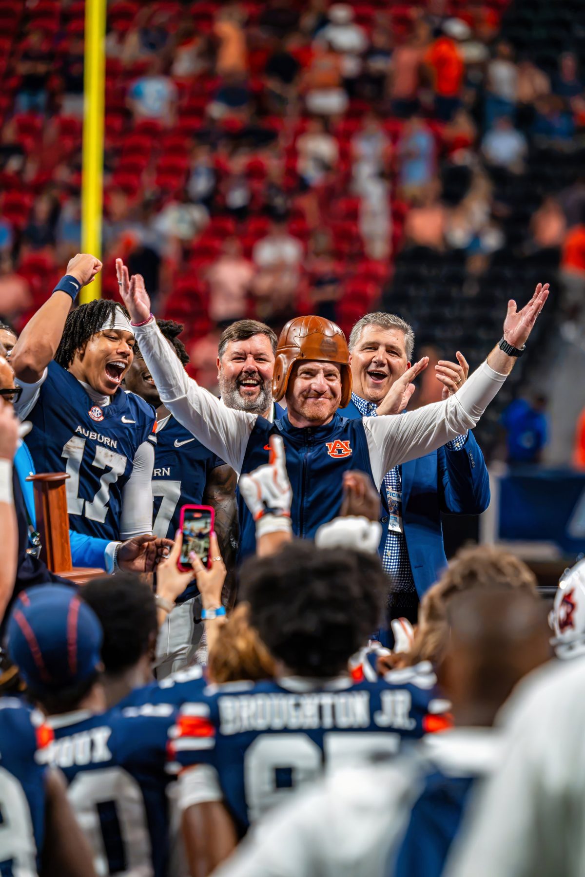Auburn players and staff celebrate on the field, one wearing a vintage leather football helmet — photo by Jimmy Warr