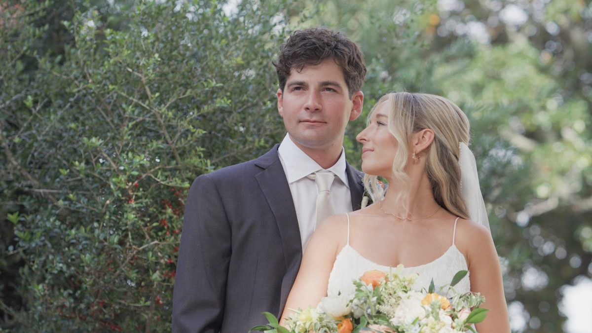 Still from the Croft Wedding film: the bride looks up at the groom, bouquet in hand, against green garden foliage — film by Jimmy Warr