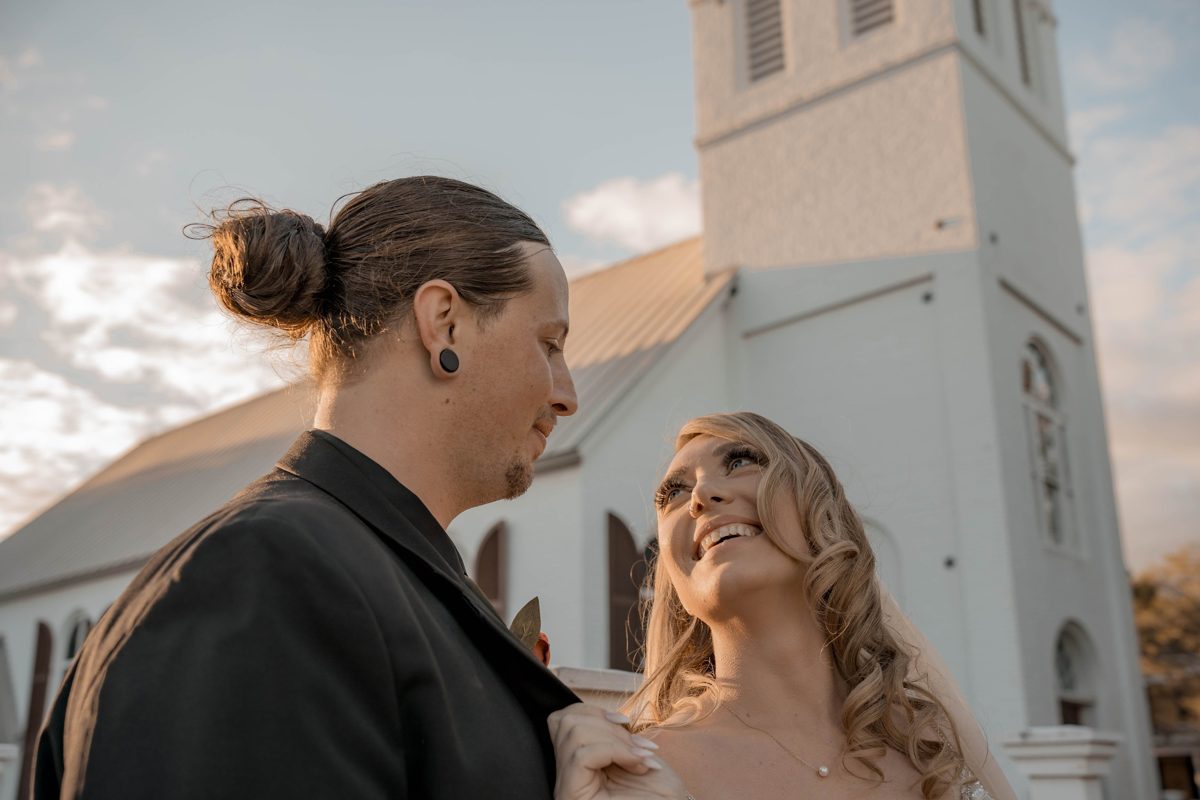 The bride smiles up at the groom in golden light, the church bell tower rising behind them — photo by Jimmy Warr