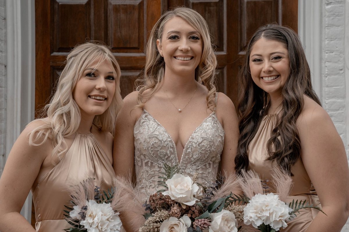The bride between two bridesmaids in front of the church's wooden doors — photo by Jimmy Warr