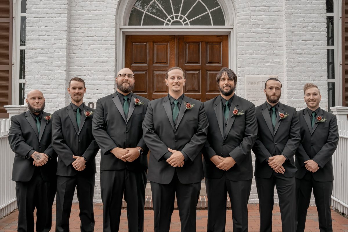 The groom and six groomsmen in black suits and green ties on the church steps — photo by Jimmy Warr