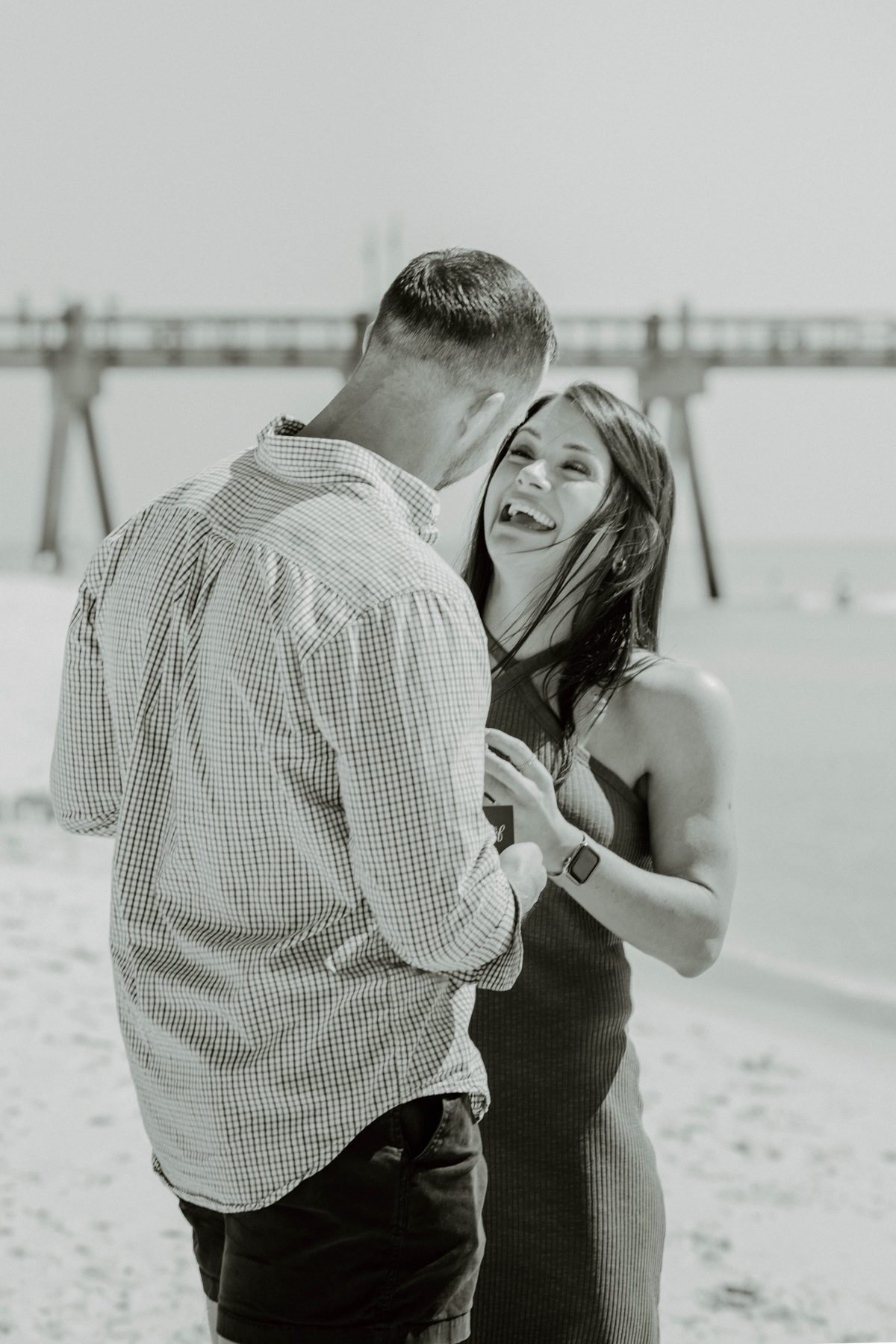 She laughs with the ring in hand, the Pensacola Beach pier soft behind them — photo by Jimmy Warr