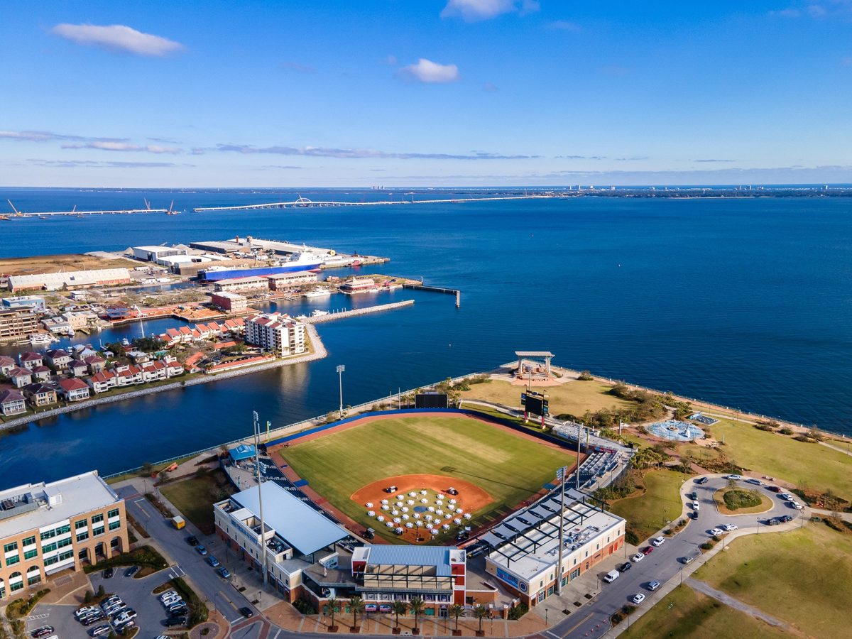 Aerial of Blue Wahoos Stadium on the Pensacola waterfront, tables set on the infield, the bay and the new Pensacola Bay Bridge beyond — photo by Jimmy Warr