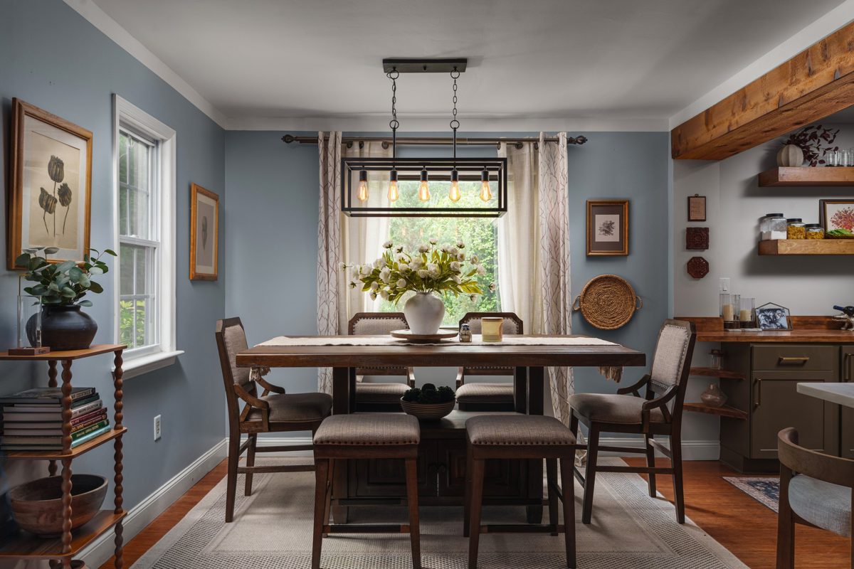 Dining room in soft blue with a five-bulb cage pendant over a counter-height table and a window full of green — photo by Jimmy Warr