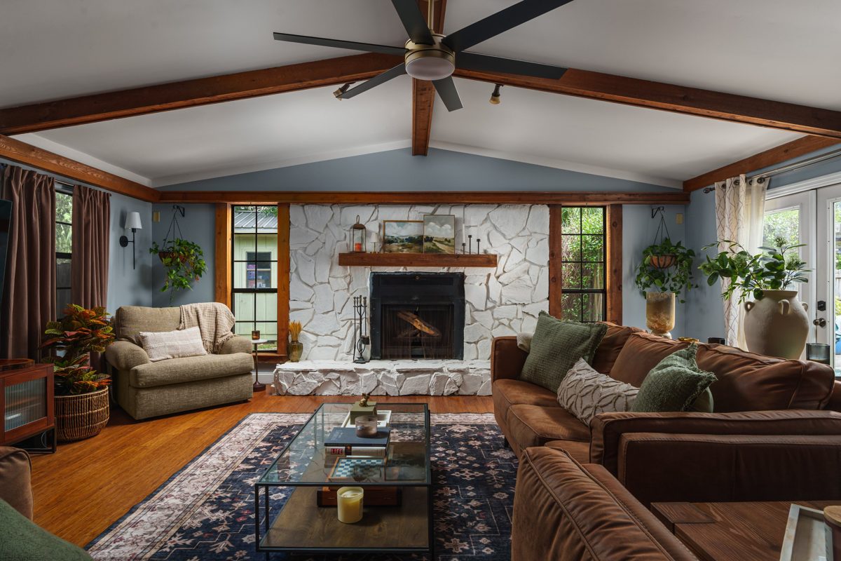 Vaulted living room with cedar beams, a white-painted stone fireplace, and leather sofas over a navy rug — photo by Jimmy Warr