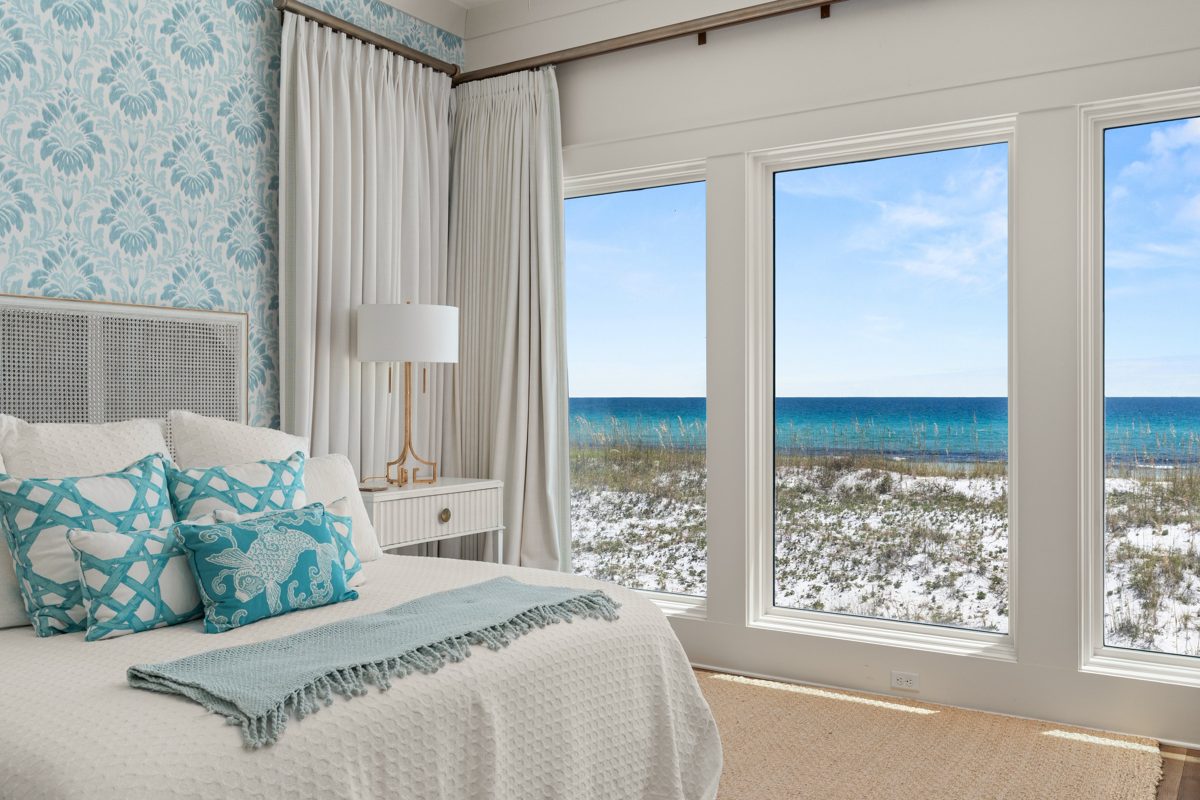 Bedroom with blue damask wallpaper and a caned headboard, floor-to-ceiling windows looking over the dunes to the Gulf — photo by Jimmy Warr