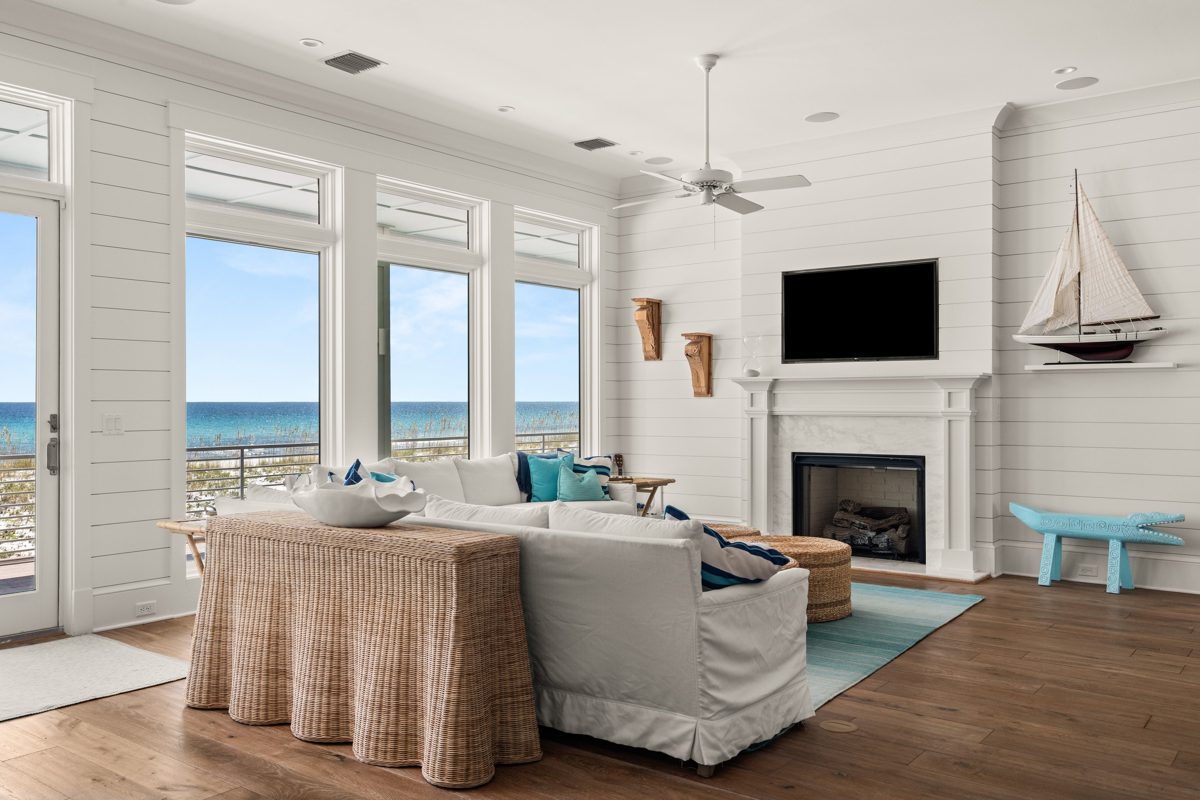 Shiplap living room with a white slipcovered sectional and wicker console, tall windows full of Gulf and sea oats — photo by Jimmy Warr