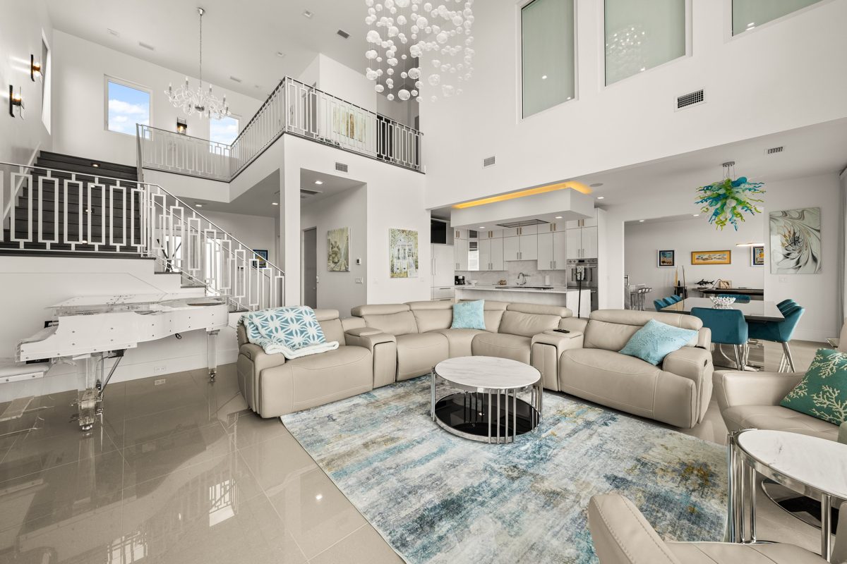 Double-height great room with a bubble-glass chandelier, a clear acrylic grand piano, and a geometric white railing up to the loft — photo by Jimmy Warr