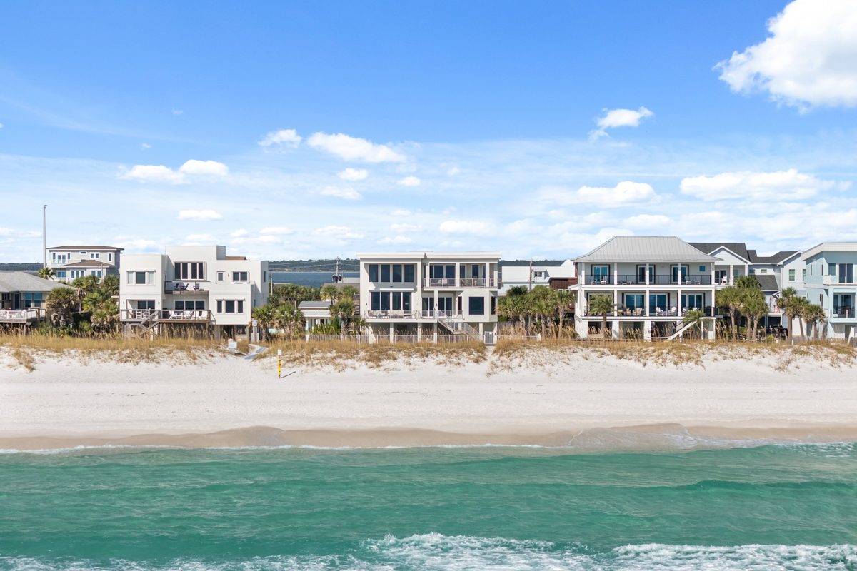 A modern white three-story home on the Gulf at Pensacola Beach, seen from over the water past sugar-white sand and sea oats — photo by Jimmy Warr