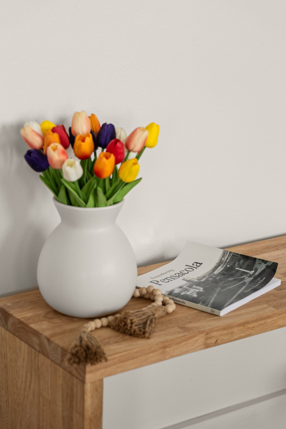 Bright tulips in a white vase on a wood console beside a book about Pensacola — photo by Jimmy Warr