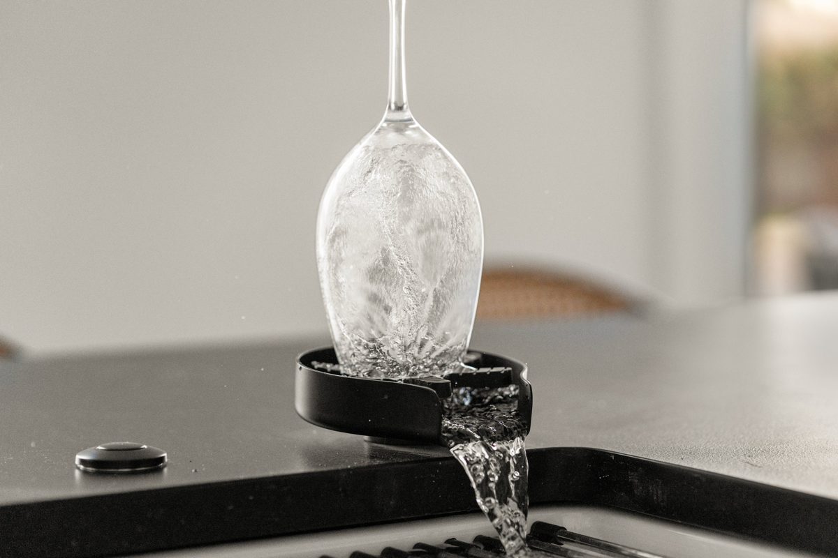 A wine glass upturned on a countertop rinser, water spilling into the sink — photo by Jimmy Warr