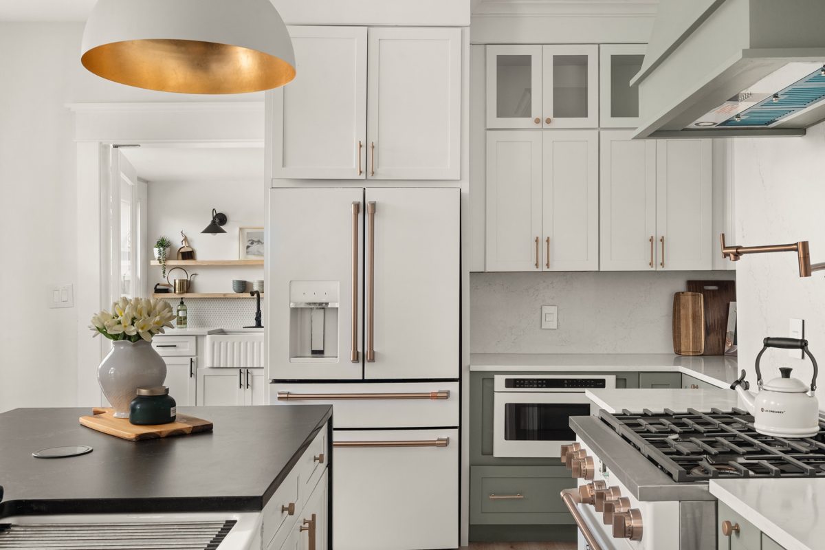 White refrigerator with copper handles framed by Shaker cabinetry, a pot filler and kettle by the range — photo by Jimmy Warr