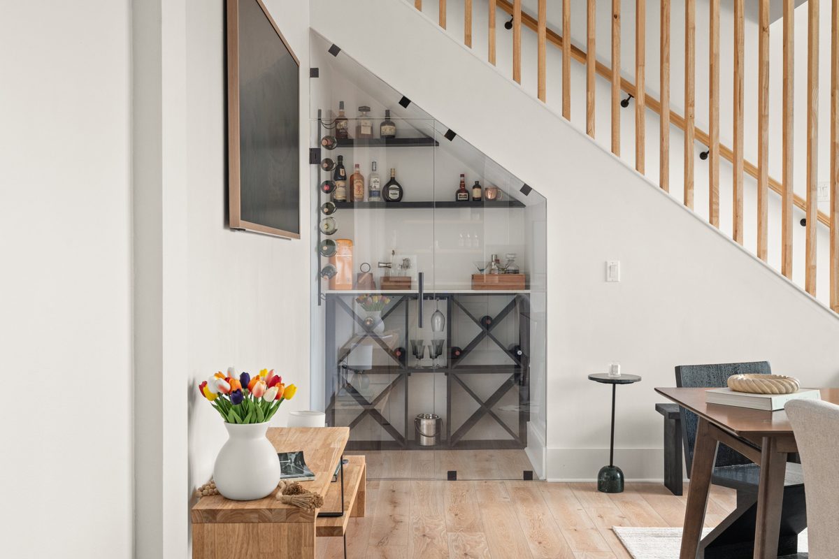 Glass-enclosed bar tucked under a staircase with wood slat railing — photo by Jimmy Warr