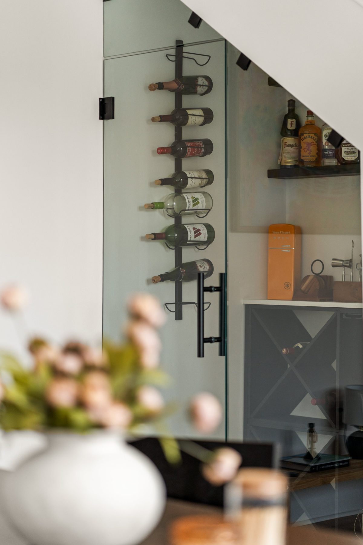 Wine bottles on a wall rack behind the glass door of the under-stair bar — photo by Jimmy Warr